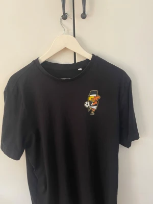 Svart AIK t-shirt med tryck - Svart t-shirt med AIK-tryck i gult på ryggen och en liten figur på bröstet fram tröjan är helt ny o endast använd en gång säljer för att den är lite stor för mig men jag vill helst att kläder ska sitta lite tight 
