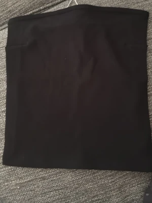 Svart tight tubtop från GinaTricot - En svart, tight kortkjol i stretchigt syntetmaterial. Enkel och clean design utan detaljer, perfekt att styla med crop tops eller oversized tröjor. Kjolen har en rak passform och är superenkel att matcha. Helt oanvänd.