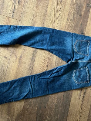 Blå jeans från Replay Wallys - Säljer ett par klassiska blå jeans från Replay, modell Wallys. Jeansen har raka ben, två bakfickor och snygga slitningar för en avslappnad look. Tillverkade i bomull med en skön passform. Perfekta till din vardagsstil!