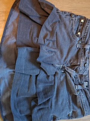 Grå volangkjol med jeanslook - Snygg grå miss me kortkjol med volangdetaljer och jeanslook. Kjolen har fickor fram, synliga sömmar och knappar i midjan. Perfekt för dig som vill ha en cool och avslappnad stil med lite edge. Priset är 400 fast kanske kan sänka beroende på köpte denna för typ 2 år sen fast har aldrig använt köpte begagnad dock och tror den är handgjord