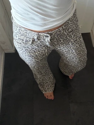 Grå leopardmönstrade jeans - Säljer ett par gråa jeans med leopardmönster och raka ben. Jeansen har klassisk femficksmodell och normal midja. Materialet känns mjukt och bekvämt, perfekt för dig som vill sticka ut med ett djurmönster i garderoben.