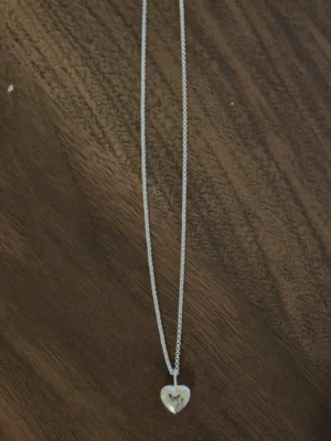 Silverhalsband med hjärthänge - Snyggt halsband i silverfärg med ett litet hjärta med en sten i som hänge. Både berlocken och kedjan är märkta med 925, vilket innebär att de är gjorda i sterlingsilver 🩷