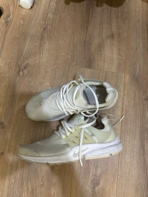 Vita Nike Prestos sneakers med mesh och plast - Säljer ett par vita Nike sneakers med mesh-ovandel och detaljer i plast. Skorna har vita snören och en låg siluett. Swoosh-logga på sidan och bekväm sula för vardagsbruk. Perfekta för dig som gillar stilrena och sportiga skor.