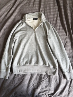 Ljusgrå halvzip sweatshirt - Snygg ljusgrå sweatshirt med halv dragkedja och hög krage. Tröjan har ribbade muddar vid ärmslut och nederkant, samt en avslappnad passform. Perfekt för en chill och stilren look. Materialet känns mjukt och bekvämt.