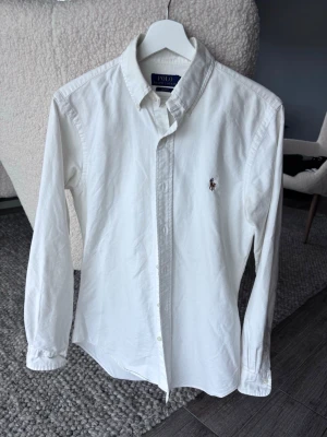 Polo Ralph Lauren skjorta - Klassisk vit skjorta från Polo Ralph Lauren med button-down krage och broderad logga på bröstet. Skjortan har långa ärmar och knäppning framtill. Perfekt till många olika stilar och enkel att matcha.
