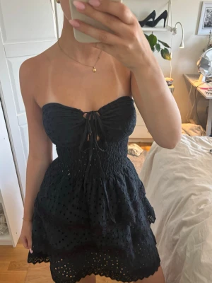 Söt svart klänning  - Söt svart axelbandslös kort klänning med broderade detaljer och volanger. Jag har aldrig använt klänningen och köpte den i Grekland, jättebra skick o inga defekter 😇😇