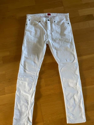 Vita slim fit jeans boss - Säljer ett par vita boss slim fit jeans med klassisk femficksdesign och raka ben. Jeansen har knappgylf och är tillverkade i ett mjukt bomullstyg med lite stretch för extra komfort. Perfekta för dig som vill ha en clean och stilren look.