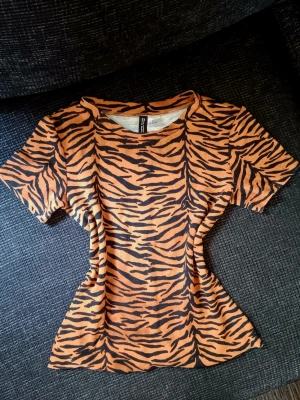 Tiger y2k t-shirt - Snygg kortärmad t-shirt med tiger mönster. T-shirten har en figurnära passform och rund halsringning. Tyget är ganska tjockt och storleken är 38 men sitter tajt och är avklippt i nederkanten så den passar perfekt på mig som har storlek 34. Den är från min mamma så jag vet inte riktigt hur använd den är men den är i bra skick och jag har aldrig använt den själv. Pris kan diskuteras 💕