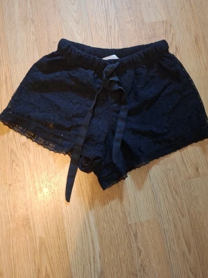 Söta svarta sköna shorts med typ blommönster på💗 - Snygga svarta shorts i spets med bred resår i midjan och dekorativ snörning framtill. Shortsen har en feminin look med spetsdetaljer längs kanterna och är perfekta för varma dagar och är jätte mjuka bara använd ett par fåtal gånger för att dom är för små storlek 146-152💗