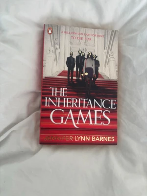 The Inheritance Games bok - En spännande skönlitterär bok på engelska, 'The Inheritance Games' av Jennifer Lynn Barnes. Omslaget är rött och vitt med mystiska figurer på en trappa. Perfekt för dig som gillar mysterier, familjehemligheter och höga insatser.