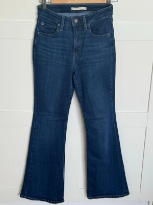 Blå bootcut jeans från Levi's - Säljer ett par klassiska blå bootcut jeans från Levi's med hög midja och fem fickor. Jeansen har en snygg tvätt och är tillverkade i ett mjukt denimtyg med lite stretch. 