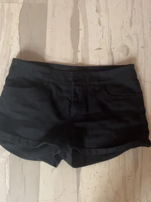 Svarta shorts med fickor - Snygga svarta shorts med klassisk femficksdesign och uppvikta benslut. Perfekta för varma dagar och enkla att matcha med olika toppar. Gjorda i ett mjukt och bekvämt bomullsmaterial med normal passform.