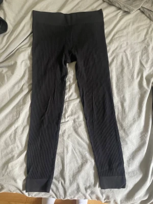 Svarta ribbade leggings från H&M - Svarta leggings från H&M med ribbad struktur och bred resår i midjan. De är långa och har en tight passform som sitter snyggt på benen. Perfekta att matcha med oversized tröjor eller hoodies för en chill look.