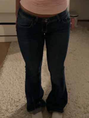 Mörkblå bootcut jeans - Säljer ett par mörkblå bootcut jeans med klassisk femficksdesign och knappgylf. Jeansen har en snygg passform som sitter tajt upptill och släpper ut vid benen. Perfekta till en trendig vardagslook.