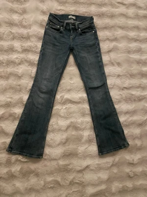 Mörkblå bootcut jeans med fickdetaljer - Säljer ett par mörkblå bootcut jeans med snygga fickdetaljer bak och klassisk femficksdesign. Jeansen har utsvängda ben och är tillverkade i ett mjukt denimtyg som sitter skönt. Perfekta för dig som gillar retrovibbar och vill ha en avslappnad men trendig look.
