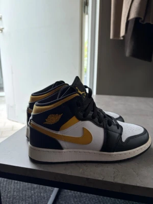 Svarta och gula Nike Air Jordan sneakers - Säljer ett par Nike Air Jordan sneakers i svart, vitt och gult. Skorna har högt skaft, klassisk Jordan-logga på sidan och gul swoosh. Tillverkade i läder med svarta skosnören och vit sula. Perfekta för dig som vill sticka ut med en ikonisk streetwear-look.