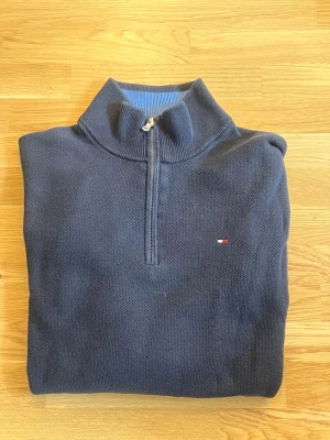 Mörkblå halvzip stickad tröja - Mörkblå vintage stickad tröja från Tommy Hilfiger med halvzip och liten logga på bröstet. Tröjan har ribbade muddar vid ärmslut och nederkant samt hög krage. Storlek L men skulle säga att den är M/L. Skriv för mer info 🙌☺️