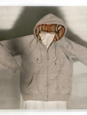 Beige hoodie med dragkedja och mönstrad huva - Säljer en beige hoodie med dragkedja och fickor framtill. Huvan har ett snyggt rutigt mönster på insidan och justerbara snören. Tillverkad i mjukt material, perfekt för chill dagar. Passar dig som gillar enkel men stilren streetwear.