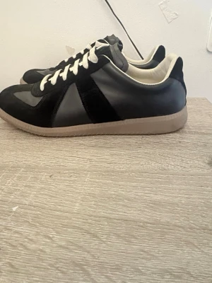 Svarta sneakers med beige sula - Stilrena svarta sneakers med beige sula och vita snören. Skorna har en kombination av mocka och slätt läder på ovandelen samt ljus insida. Klassisk låg modell som passar till många olika outfits.