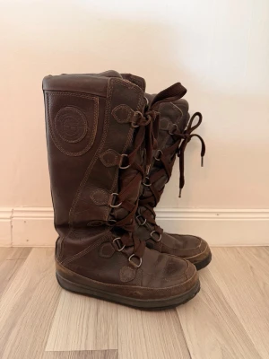 Bruna höga läderstövlar Timberland - Snygga bruna höga stövlar från Timberland i äkta läder. Stövlarna har grova snörningar framtill, robust sula och dekorativa sömmar. Perfekta för dig som vill ha en cool och tidlös look med outdoor-vibe.