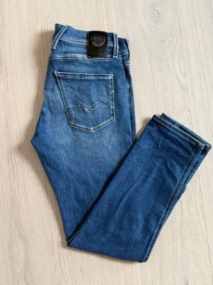 Replay Anbass - Snygga blå slim fit jeans från Replay med klassisk femficksdesign och lätt slitna detaljer på låren. Jeansen har normal midja, raka ben och är gjorda i mjukt denimtyg med stretch för extra komfort. Perfekta till en avslappnad och trendig look.