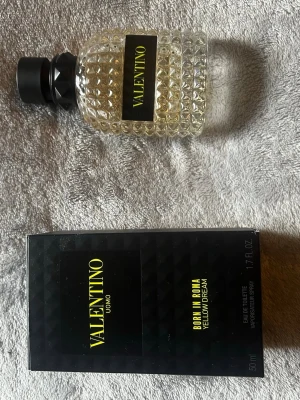 Valentino Born In Roma Yellow Dream - Valentino Born In Roma Yellow Dream Uomo är en parfym i en lyxig, transparent glasflaska med nitar och svart lock. Flaskan har en modern design med gul text på svart etikett. Förpackningen är svart med gul text och rymmer 50 ml eau de toilette.