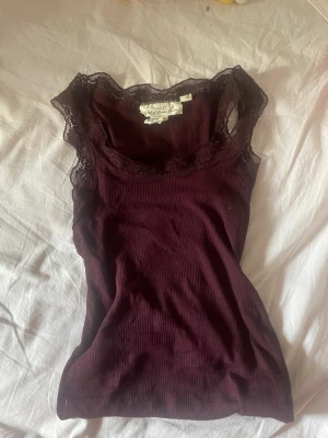 Lila ribbad linnetopp med spets - Supersnygg vinröd ribbad linnetopp från HM med spetsdetaljer runt ringningen och axelbanden. Perfekt att styla lager på lager eller bära som den är. Mjuk och stretchig.