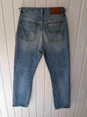 Ljusblå raka jeans, modell MEG - Säljer ett par ljusblå jeans i modellen MEG med raka ben och klassiska bakfickor. Jeansen har snygga slitningar och kontrastsömmar. Tillverkade i bomull och perfekta för en avslappnad stil.
