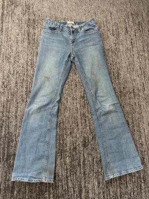 Ljusblå bootcut jeans - Säljer ett par ljusblå bootcut jeans med klassisk femficksdesign och snygga detaljer på bakfickorna. Jeansen har normal midja och är tillverkade i mjuk denim med lätt tvättad look. Perfekta för dig som gillar retrovibbar och avslappnad stil.
