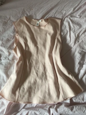 Ljusbeige ärmlös topp - Säljer en stilren ljus rosa topp i ett mjukt material. Toppen är ärmlös med rund halsringning och har en lätt utsvängd passform som ger en snygg siluett. Perfekt att matcha med jeans eller kjol för en clean look.