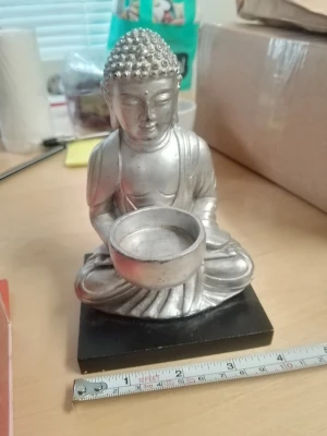 Silverfärgad Buddha staty - Dekorativ Buddha staty i silverfärgad metall som sitter i meditationsställning och håller en skål. Statyn står på en svart fyrkantig bas och är cirka 15 cm hög. Perfekt som inredningsdetalj för att skapa en lugn och harmonisk känsla i rummet.