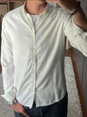 Les Deux skjorta i créme - stl M - Skjorta från Les Deux i lyocell (Tencel), svalt och mjukt tyg med bra fall. Button down-krage och rak passform, skön nu i sommarvärmen. Personen på bilden är 189cm, väger 78kg.  Använd men i mycket fint skick, inga hål eller fläckar.  Rök- och djurfritt hem. Skriv gärna om du vill ha fler bilder eller undrar något!