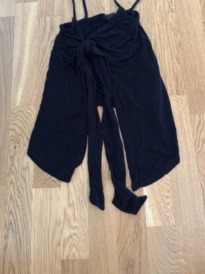Svart linnetopp med knyt från Gina Tricot - Svart linnetopp från Gina Tricot med smala axelband och snygg knytning framtill. Toppen är ärmlös och har en croppad passform som passar perfekt till höga jeans eller kjol. Tillverkad i mjukt bomullsmaterial.