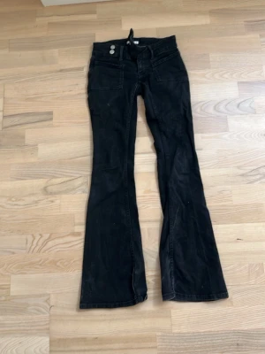 Svarta bootcut jeans med detaljer - Snygga svarta bootcut jeans med dubbla knappar i midjan och dekorativa sömmar. Baksidan har fickor med glittriga mönster som ger extra attityd. Perfekta för dig som gillar en retroinspirerad look och vill sticka ut lite extra.