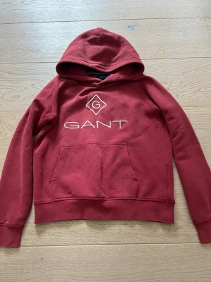 Vinröd hoodie från GANT med logga - Säljer eftersom den är för liten, är i bra skick, den har däremot någon vit fläck längt ner på ärmen och en som syns på sista bilder. Utöver detta är den bra!