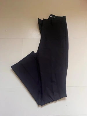 Svarta kostymbyxor från BikBok - Snygga svarta kostymbyxor från BikBok med raka ben och klassisk passform. Byxorna har hällor för skärp och diskreta sidofickor. Perfekta för en stilren och trendig look. Materialet känns mjukt och följsamt.