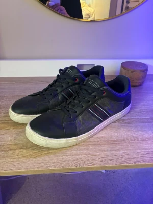 Svarta race marine  sneakers - Snygga svarta sneakers med vita sulor och diskreta ränder i rött och vitt på sidan. Skorna har svarta skosnören, meshdetaljer på sidorna och röda detaljer vid snörningen. Perfekta för en avslappnad och trendig look.