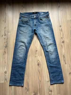 Blå raka jeans från replay - Säljer ett par klassiska blå jeans med raka ben och snygga slitningar framtill. Jeansen har fem fickor, dragkedja och knapp i midjan samt detaljerade sömmar på bakfickorna. Perfekta för en avslappnad och trendig look.