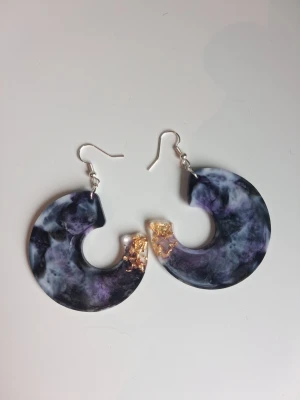  marmorerade örhängen handgjorda resin/epoxy - Unika handgjorda örhängen,marmorerat mönster i lila, svart och vitt. Dekorerade med guldfärgade detaljer för extra effekt. Tillverkade i resin/epoxy. Perfekta för dig som vill sticka ut med accessoarerna. Öronkroken är nickelsäker längd ca 5.5cm