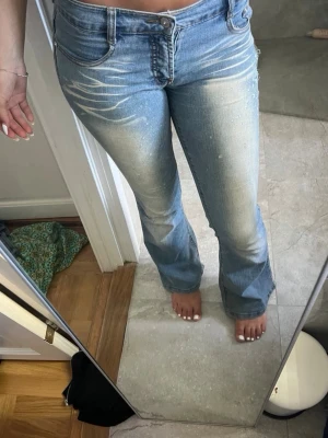 Ljusblå bootcut jeans med slitningar - Säljer ett par ljusblå bootcut jeans med snygga slitningar och blekta detaljer framtill. Jeansen har klassisk femficksmodell och normal midja. Perfekta för en avslappnad och trendig look.