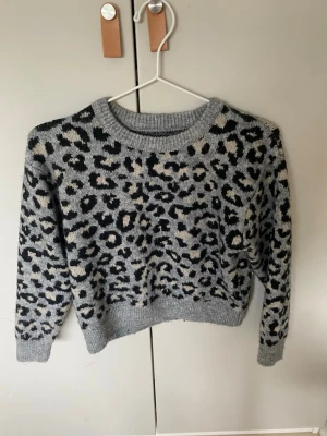 Grå leopardmönstrad stickad tröja - Säljer en stickad tröja i grått med leopardmönster i svart och beige. Perfekt för dig som vill ha en trendig och mysig look. Använd väldigt få gånger!