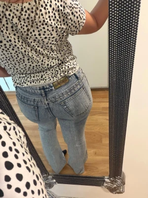Ljusblå bootcut jeans med tvättad look - Säljer ett par ljusblå bootcut jeans med tvättad effekt och medelhög midja. Jeansen har dubbla knappar framtill, klassiska fickor och en snygg retrovibe. Materialet är denim i bomull och passformen är figurnära upptill med utsvängda ben.