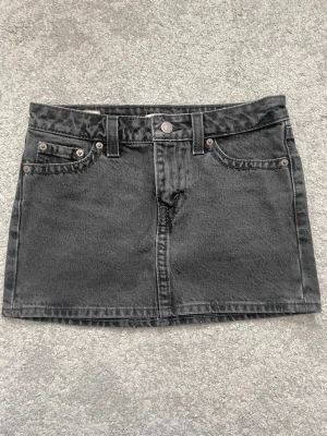 Svart jeanskjol från Levi’s - Snygg svart jeanskjol i kort modell med klassiska fem fickor, bälteshällor och knappstängning fram. Kjolen har en cool tvättad look och bakfickor med knapp. Perfekt till vardags för en trendig och avslappnad stil. Använd typ 1-2 gånger för den är för liten för mig