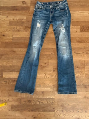 Blå slitna bootcut jeans Miss Me - Säljer ett par blå bootcut jeans från Miss Me med slitningar och hål på båda benen. Storlek 28 med 86cm i innebenslängd och 37cm i midjan (tvärs över). Säljer då de tyvärr ej kommer till användning längre.