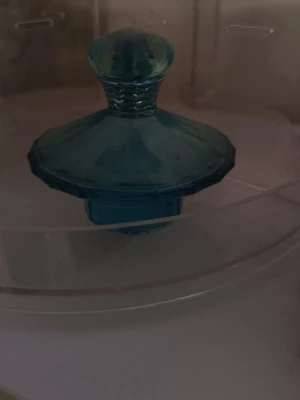 Curious av Britney Spears. Parfym  - Säljer en unik parfymflaska i blått glas med en elegant, rundad form och dekorativ kork. Flaskan har en vintagekänsla och är perfekt som inredningsdetalj eller för din favoritdoft. Passar dig som gillar snygga och annorlunda flaskor.