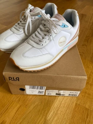 Vita sneakers från Palpa - Snygga vita sneakers från Palpa med detaljer i ljusrosa, beige och blått. Skorna har klassisk låg profil och en mix av läder,tyg och mocka i materialet. De är i gott skick.