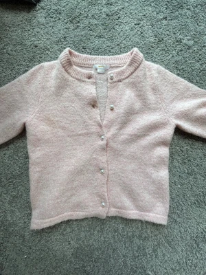 Ljusrosa kofta från Gina Tricot - Supersöt ljusrosa kofta från Gina Tricot med pärlknappar framtill. Koftan är stickad i mjukt material. Koftan är från Gina Young och jag säljer pågrund av att den är för liten. Använd några gånger väldigt bra skick! 