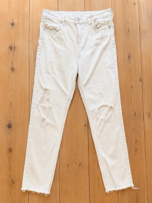 Ljusa distressed jeans med råa kanter - Säljer ett par ljusa jeans med slitna detaljer och hål på båda benen. Jeansen har fem fickor, hög midja och raka ben med råa, fransiga benslut. Perfekta för en avslappnad och trendig look. Passar mig som normalt har 38