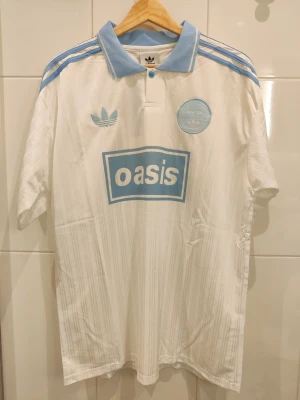 Oasis turnétröja 25' - L - Säljer en Oasis turnétröja / fotbollströja för deras turné 2025 i storlek L. Tröjan är en reprint helt ny och oanvänd. Vit tröja med ljusblåa detaljer.