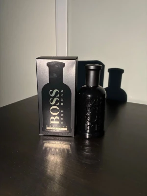 Hugo Boss Bottled parfym 100ml - En elegant parfym från Hugo Boss i en matt svart flaska med tydlig logga. Doften har toppnoter av mandarin och rökelse, hjärtnoter av iris och fikon samt basnoter av cederträ och vegetabiliskt läder. Flaskan har en stilren, maskulin design och kommer i originalkartong.